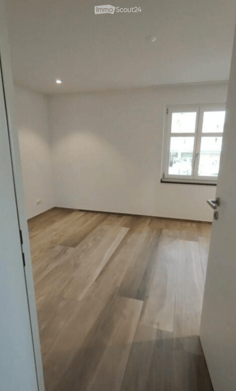 Empty room with wooden flooring and white walls, featuring a window and a door.