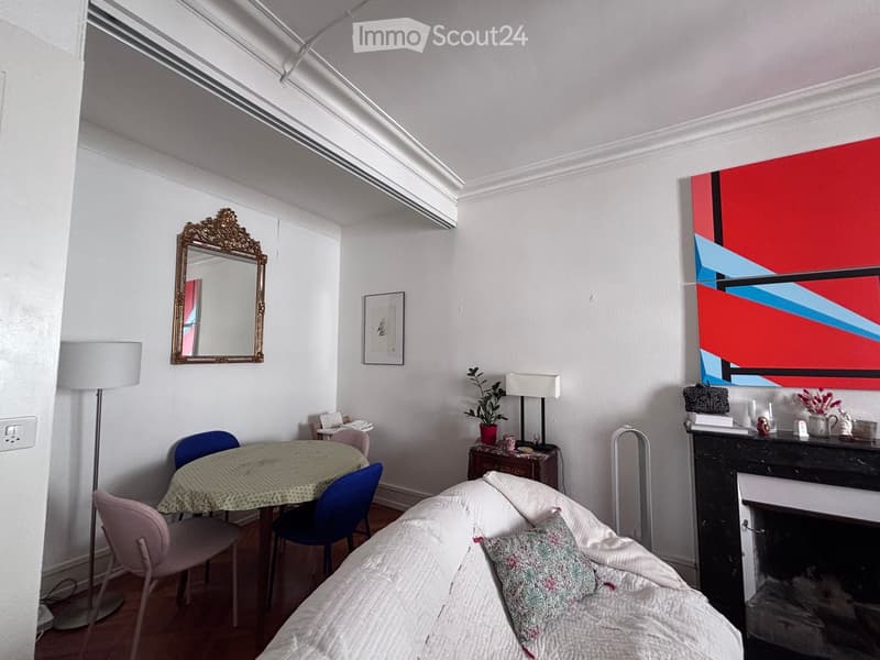 A cozy living room with a sofa, a small dining table with chairs, a fireplace, a mirror, and decorative artwork.