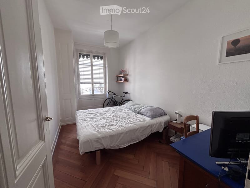 A small, furnished bedroom with a bed, a chair, a table, a screen, a bicycle, and a shelf.