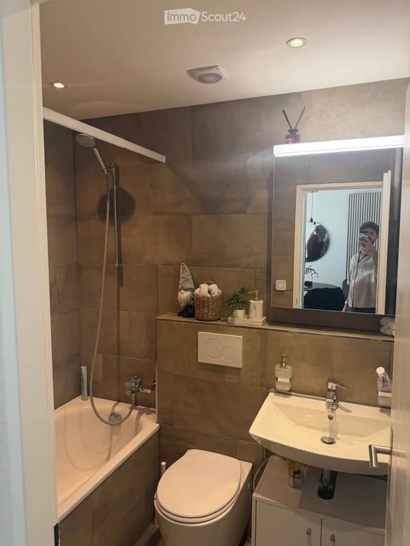 Modern bathroom with a bathtub, toilet, sink, and large mirror. Includes a wicker basket with towels and a small plant on the counter.