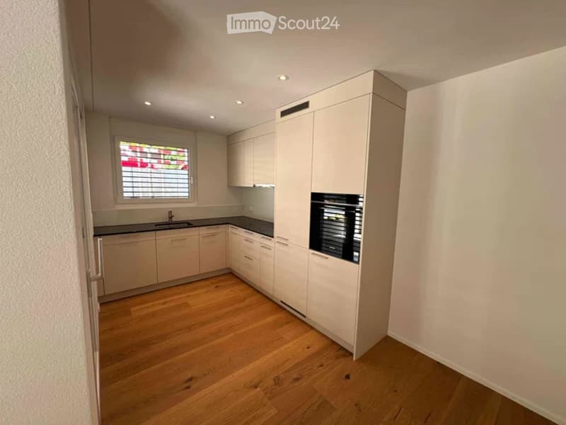 Modern kitchen with light-colored cabinets, a window with blinds, and a wooden floor.