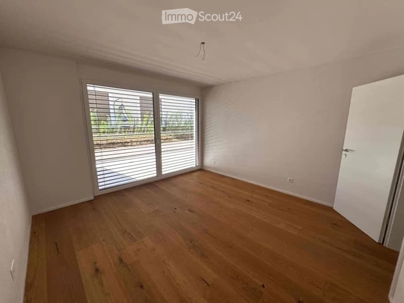 Empty room with wooden flooring, large sliding glass doors, and white walls.