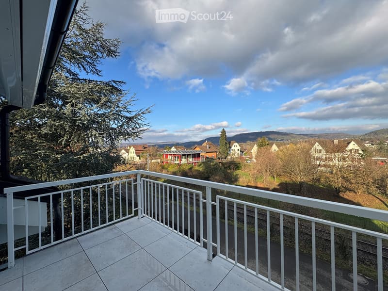 Balcony with white railing, tiled floor, overlooking a residential area with trees and houses.