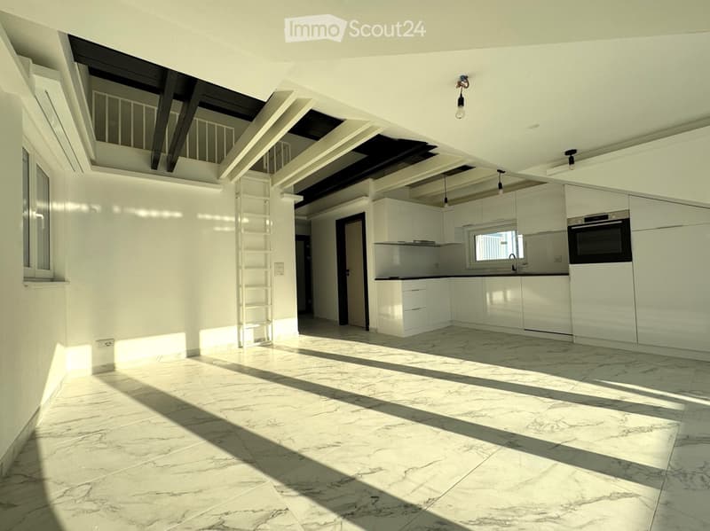 Bright, modern kitchen with white cabinets, marble flooring, and built-in oven. Natural light streams in from large windows, creating a clean and airy atmosphere.