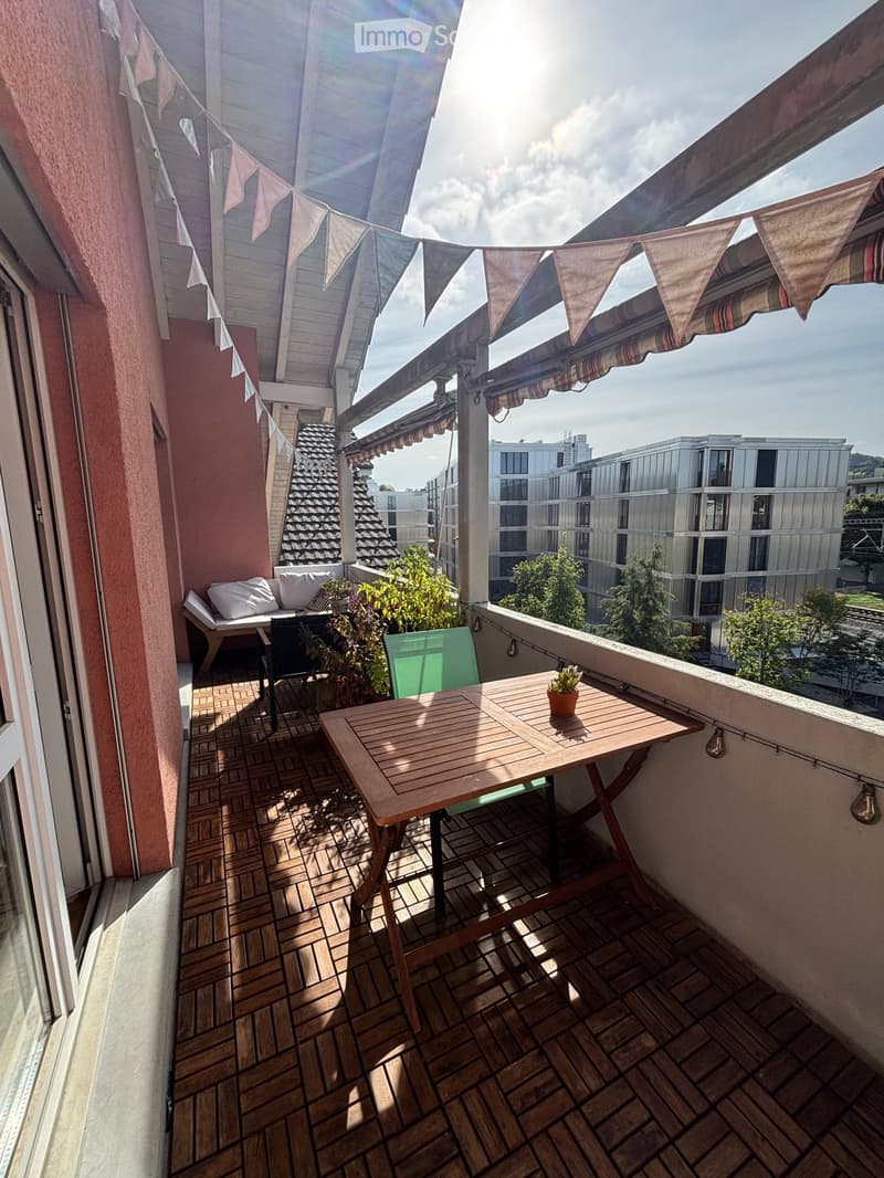 Balcony with wooden decking, a small table with a potted plant, a chair, and a sofa with cushions.