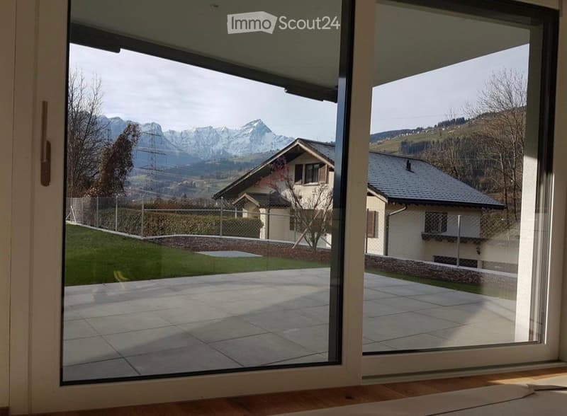 Large sliding glass doors open to a tiled balcony with a scenic mountain view and a well-maintained lawn.