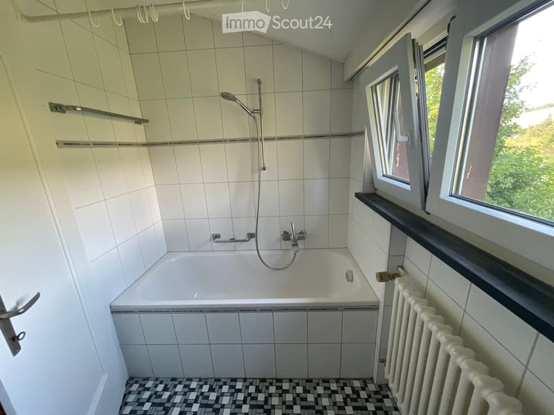 Bathroom with a bathtub, shower, radiator, and window with a view of greenery.