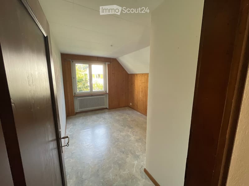Empty attic room with wooden walls, concrete floor, and a window letting in natural light. No furniture or equipment is present.