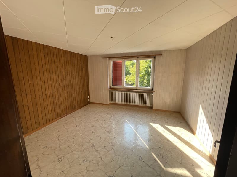 Empty room with wooden panel walls, tiled floor, and a window with a radiator below it.