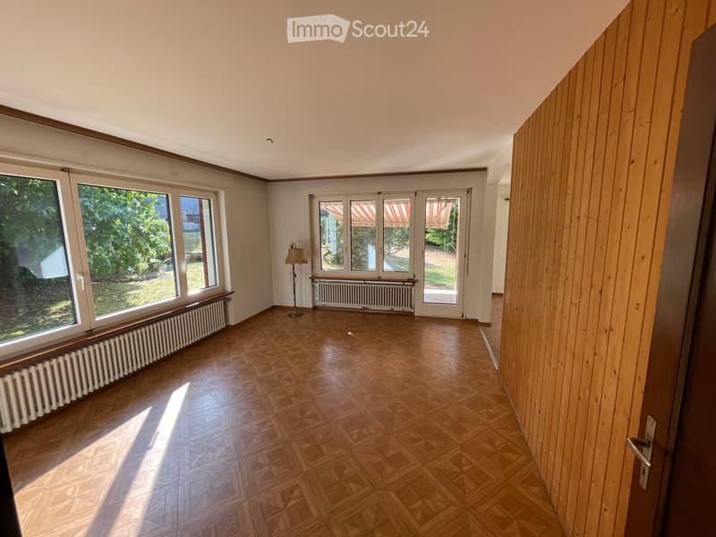 Empty room with wooden parquet flooring, large windows, radiators, and a single floor lamp.