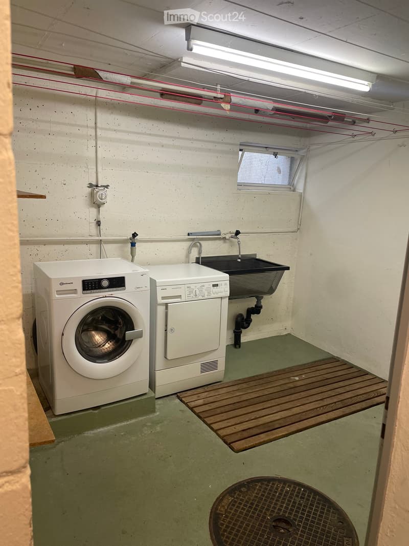 Utility room with a washing machine, dishwasher, and sink, featuring a concrete floor and exposed pipes.