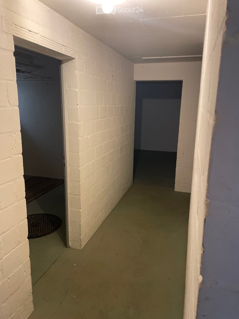 Empty hallway with white brick walls, green floor, and two open doorways leading to other spaces.