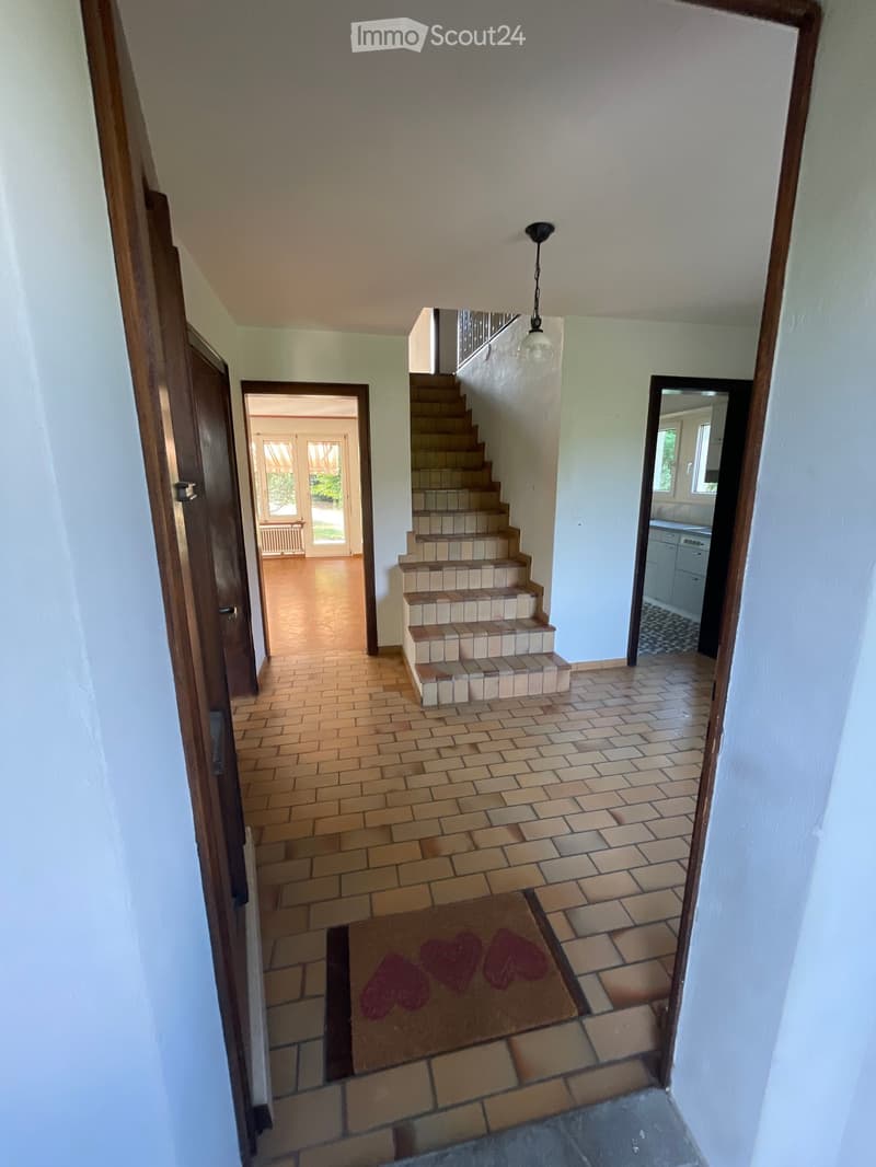Hallway with tiled floor, wooden doors, staircase leading upstairs, and a small rug with heart designs.