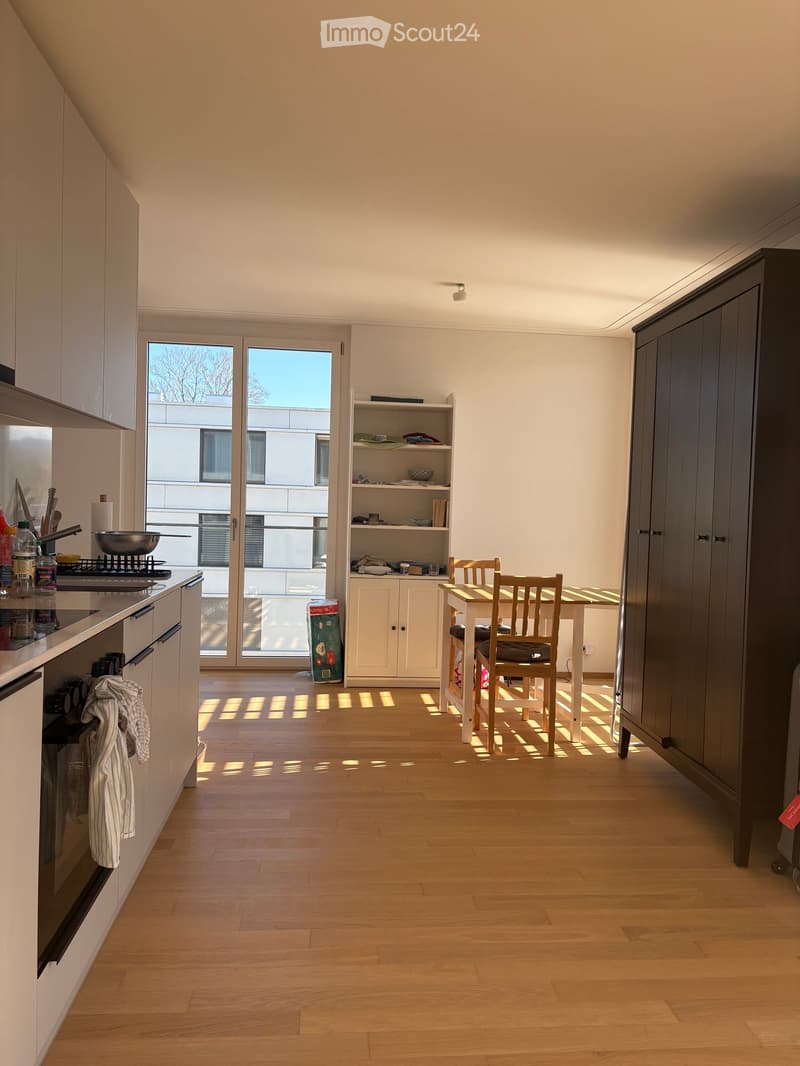 Open-plan kitchen and dining area with light wooden flooring, white cabinets, a small dining table with chairs, and a windowed door leading outside.