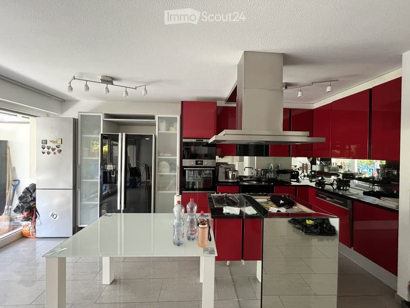Modern kitchen with red cabinets, stainless steel appliances, and a central island with a glass table and bottles.