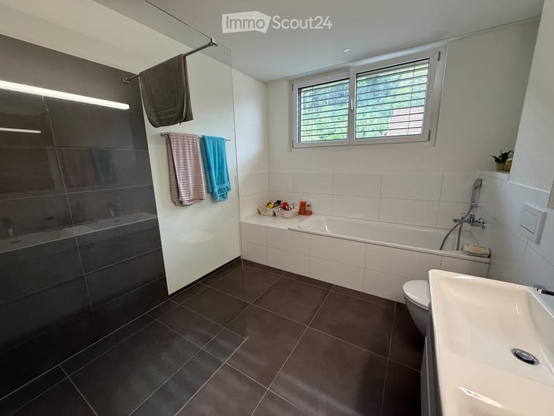 Modern bathroom with dark tiled floor, white tiled walls, bathtub, toilet, sink, shower, and towels.