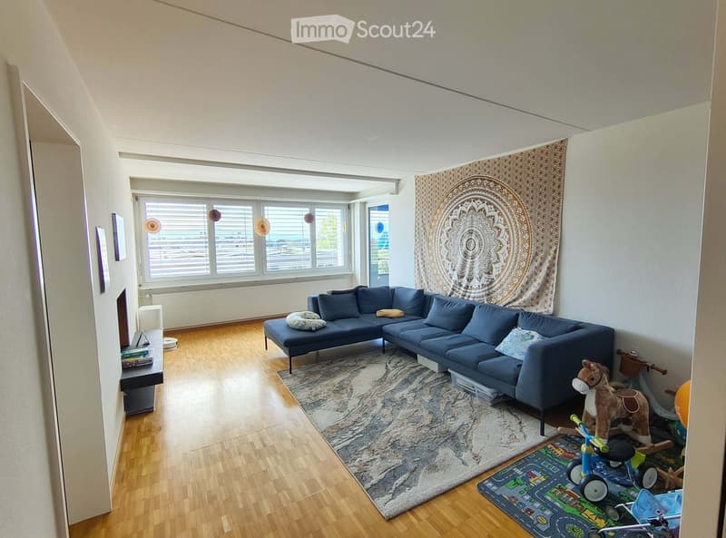 Living room with a blue sectional sofa, a large circular tapestry, a patterned rug, and various children's toys including a toy horse and a toy car.