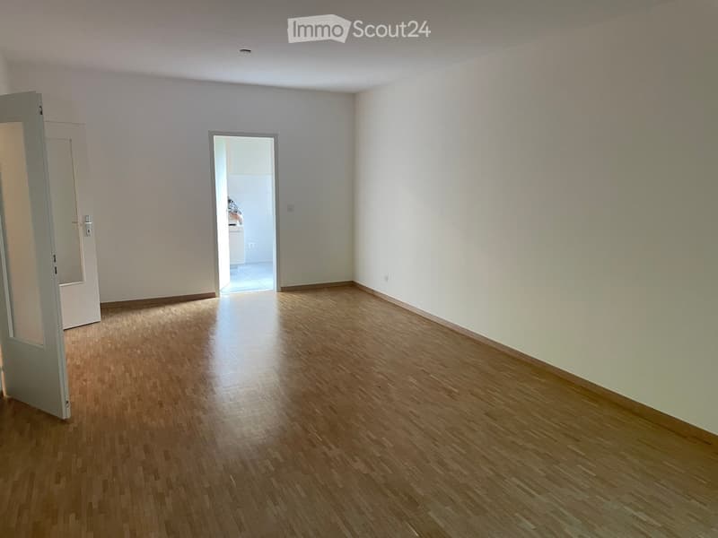 Empty room with wooden flooring and white walls, featuring an open doorway leading to another room.