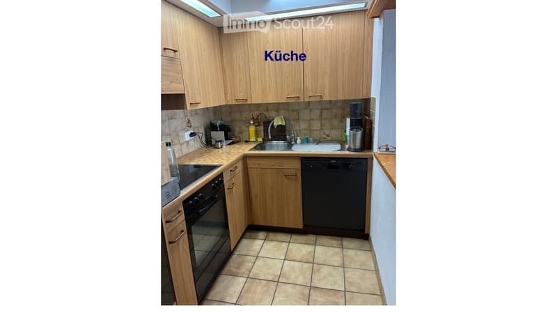A modern kitchen with light wooden cabinets, tiled floor, and various appliances including an oven, dishwasher, and coffee maker.