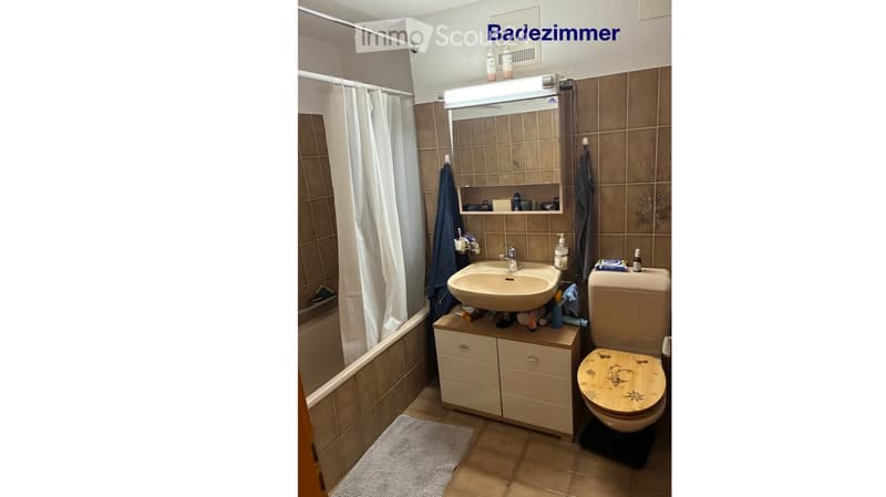 Bathroom with a bathtub, sink, toilet, mirror, and cabinet. The walls are tiled, and there is a towel hanging on the side.