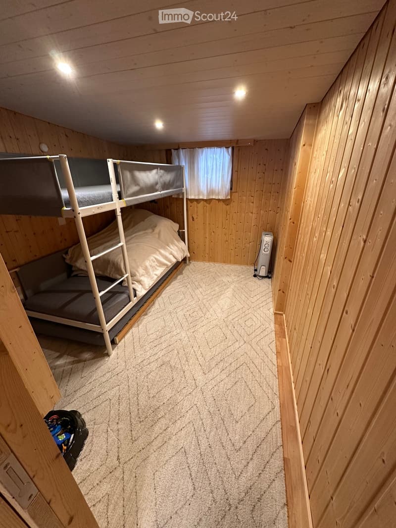 Cozy wooden bedroom with a bunk bed, white bedding, and a small heater near the window.