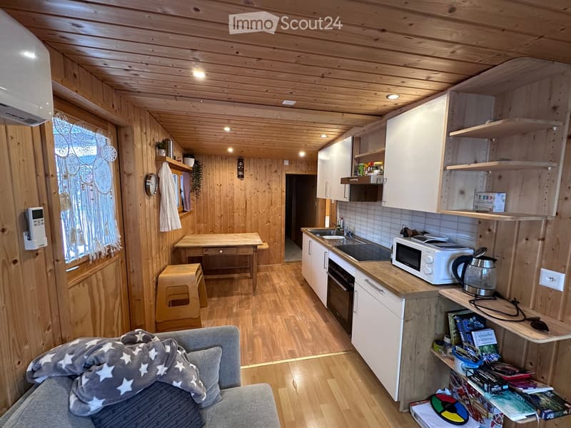 Cozy wooden interior with a sofa, small table, stool, microwave, oven, sink, fridge, and shelves with books and items.