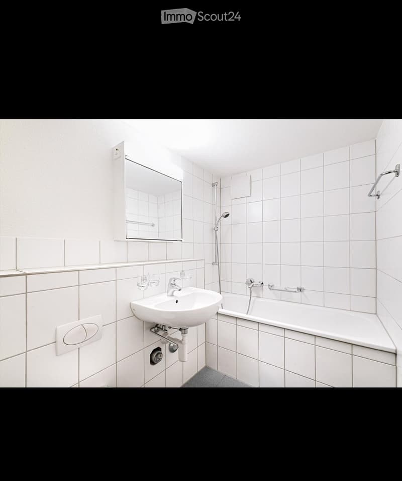 Modern bathroom with white tiled walls and floor, featuring a sink, bathtub, mirror, and showerhead.