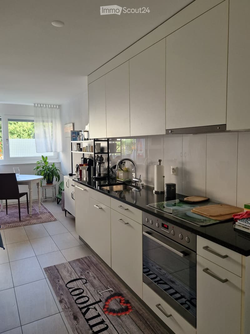Modern kitchen with white cabinets, black countertops, stainless steel appliances, and a small dining area with a table and chair.