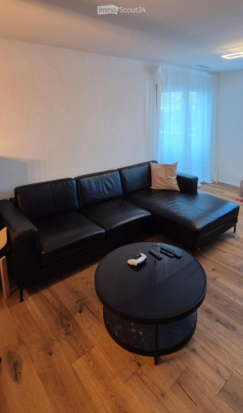 Modern living room with a black leather sectional sofa, a round black coffee table, and wooden flooring.