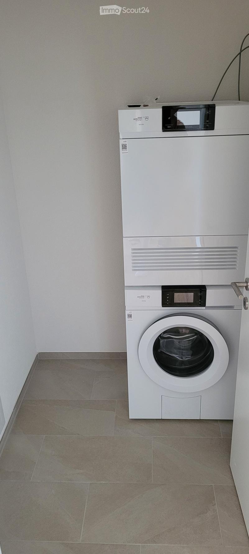 A small bathroom with a tiled floor and white walls, featuring a stacked washing machine and dryer unit.