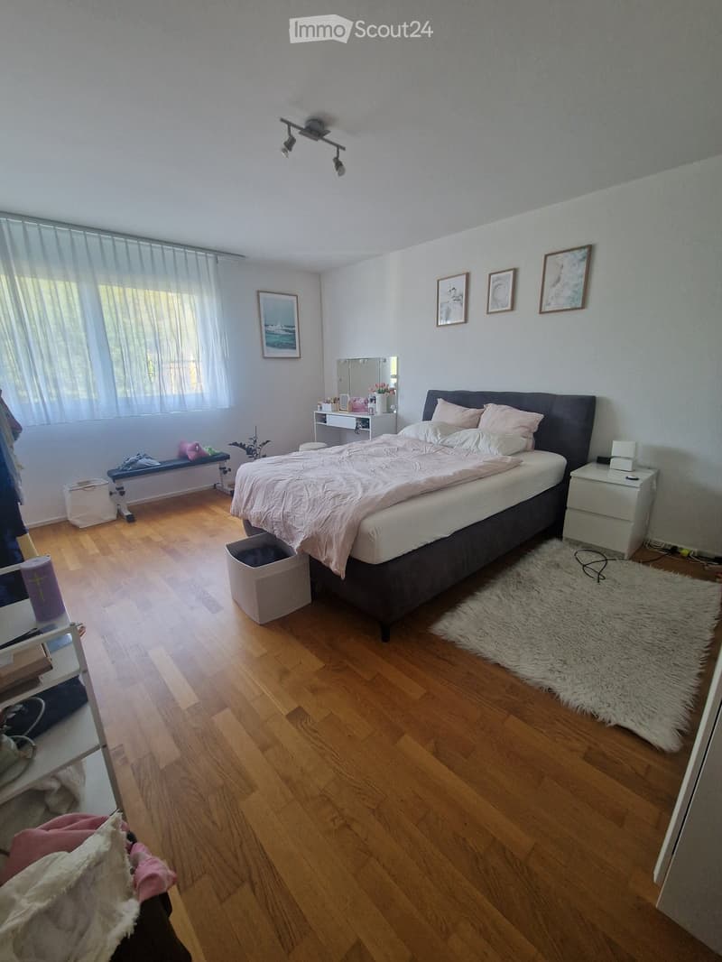 Cozy bedroom with wooden flooring, large bed with pink bedding, nightstand, mirror, bench, and artwork on the walls.