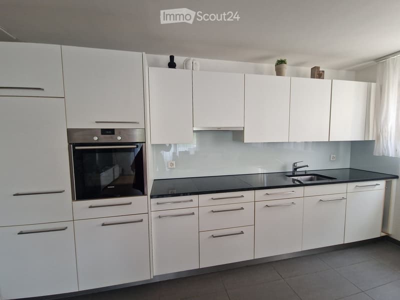 Modern kitchen with white cabinets, stainless steel oven, black countertop, and sink.