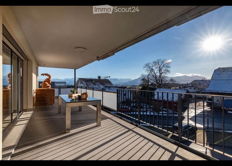 Balcony with a view of mountains, featuring a table, chairs, a plant, and a decorative sculpture.