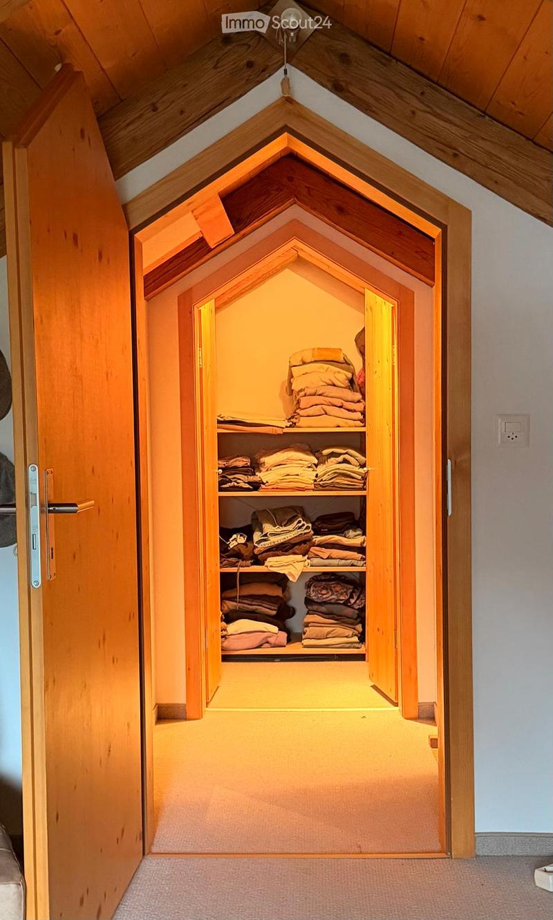 A well-lit, wooden closet with multiple shelves filled with neatly stacked blankets and linens, featuring a sloped wooden ceiling and warm ambient lighting.