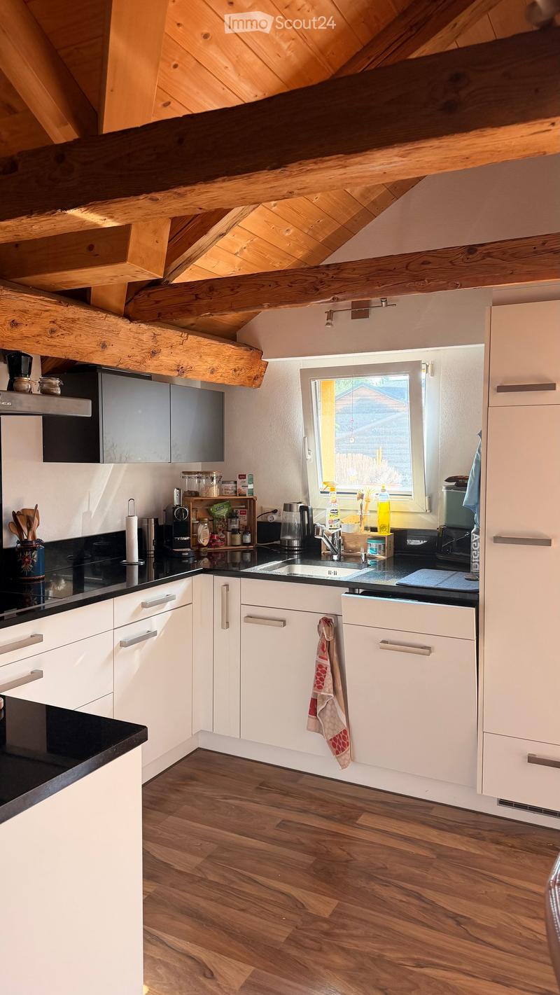 Modern kitchen with white cabinets, wooden floor, black countertops, and various appliances including a sink, oven, and coffee maker.
