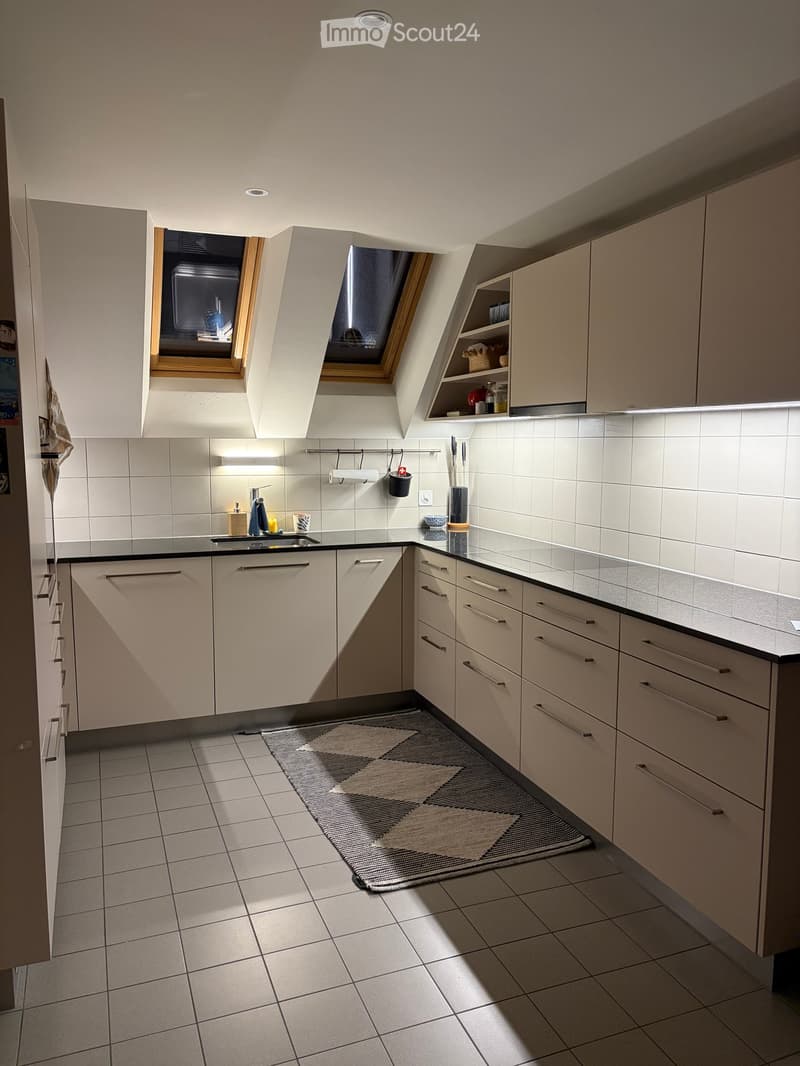 Modern kitchen with white cabinets, black countertops, and a small rug on the floor. Features include a sink, faucet, and various small items on the counter.