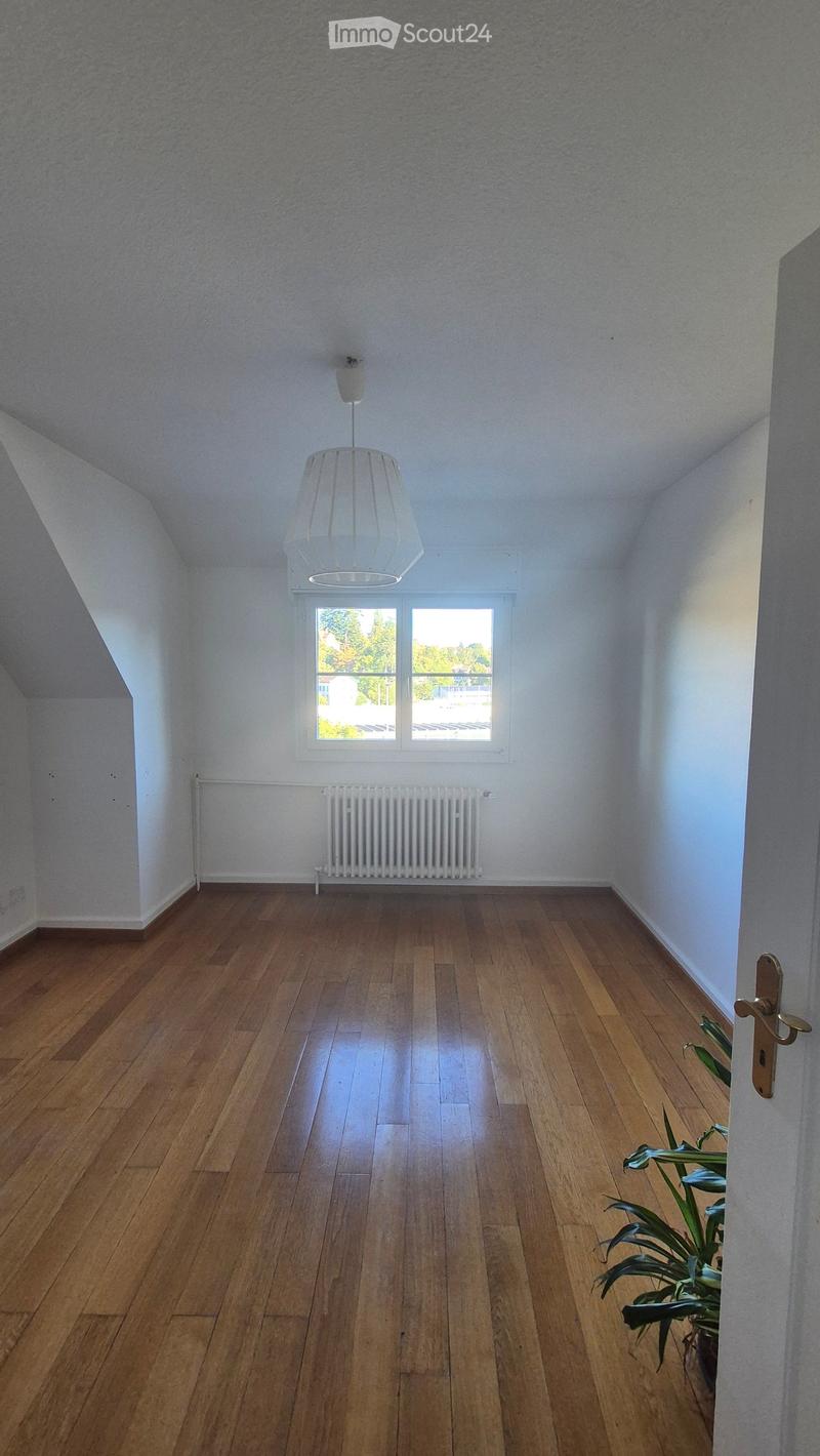 Empty room with wooden flooring, white walls, a window with a view, a radiator, and a hanging light fixture.