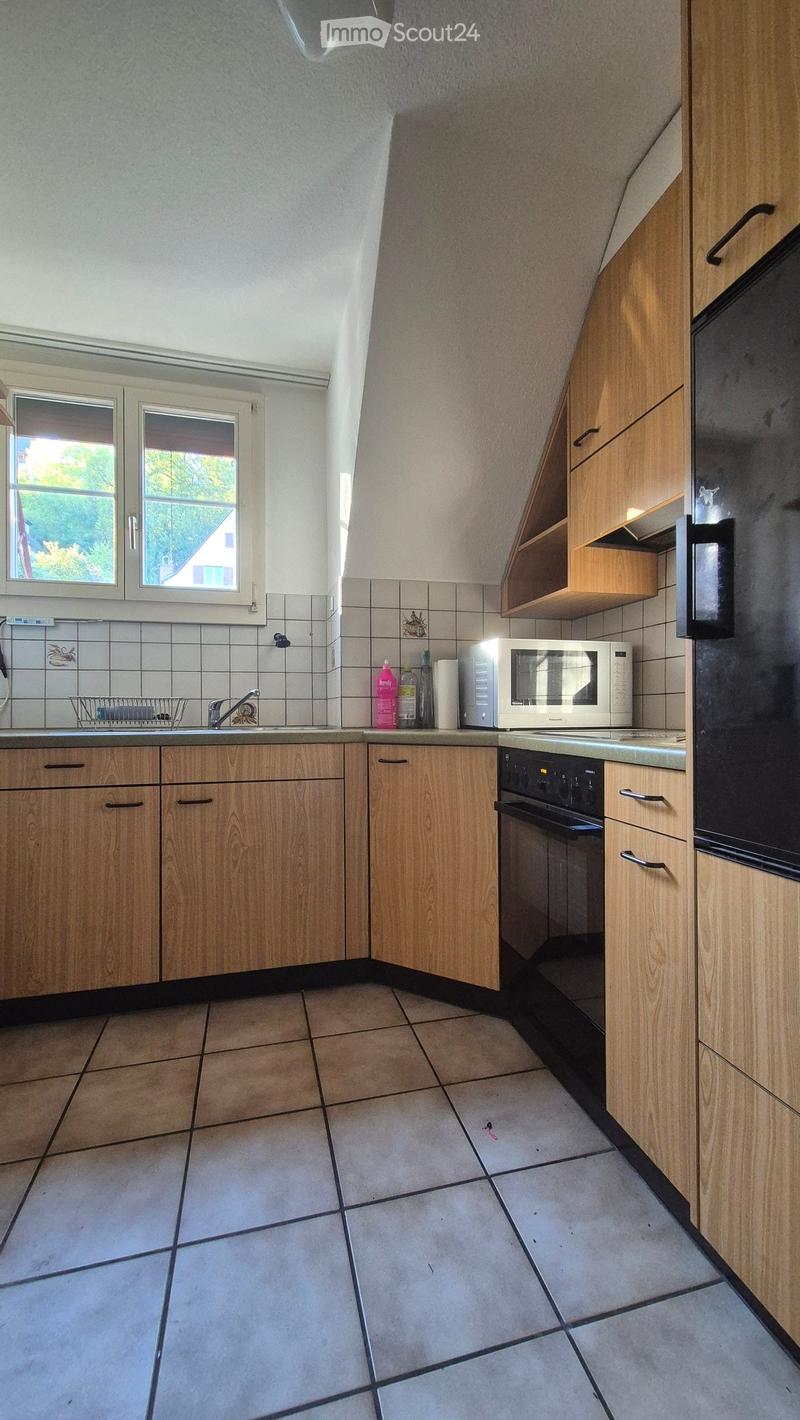 Kitchen with wooden cabinets, tiled floor, sink, microwave, oven, refrigerator, and a window with a view of greenery.