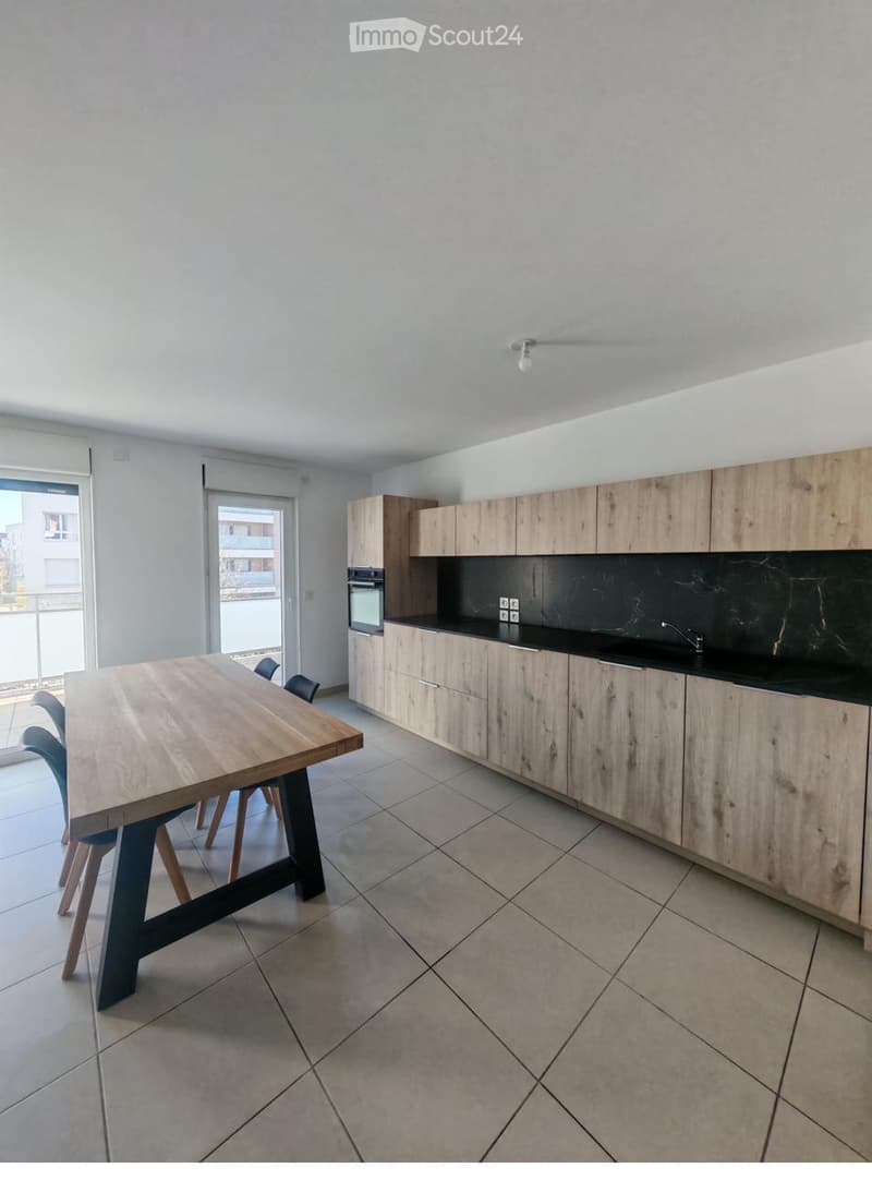 Modern kitchen with light wooden cabinets, black countertops, a wooden dining table with chairs, and an oven.
