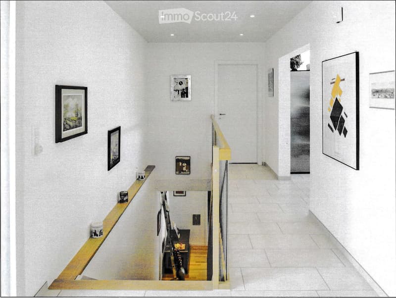 Modern hallway with white walls, framed artwork, and a glass-enclosed staircase leading to another level.