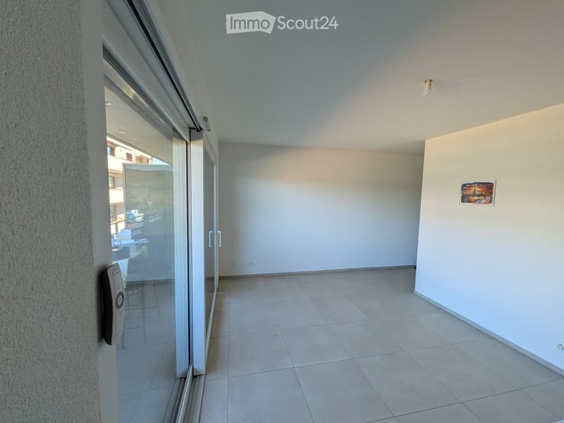 Empty room with tiled floor, white walls, large glass sliding door leading to an outdoor area, and a small artwork on the wall.