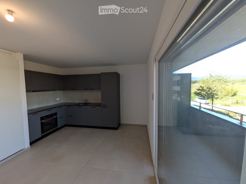 Modern kitchen with grey cabinets, tiled floor, and large window overlooking a scenic landscape.