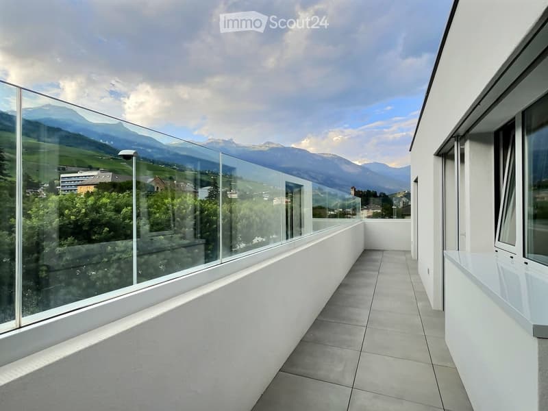 Modern balcony with large glass railings, tiled floor, and scenic mountain view.