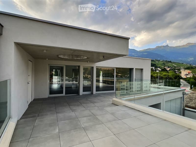 Modern balcony with tiled floor, glass railings, and large sliding glass doors leading to the interior. Offers a scenic view of mountains and countryside.