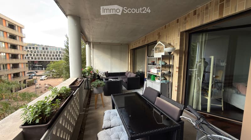 Balcony with outdoor furniture including a sofa, table, chairs, potted plants, and a cat tree. The balcony has a modern design with a view of a cityscape and greenery.