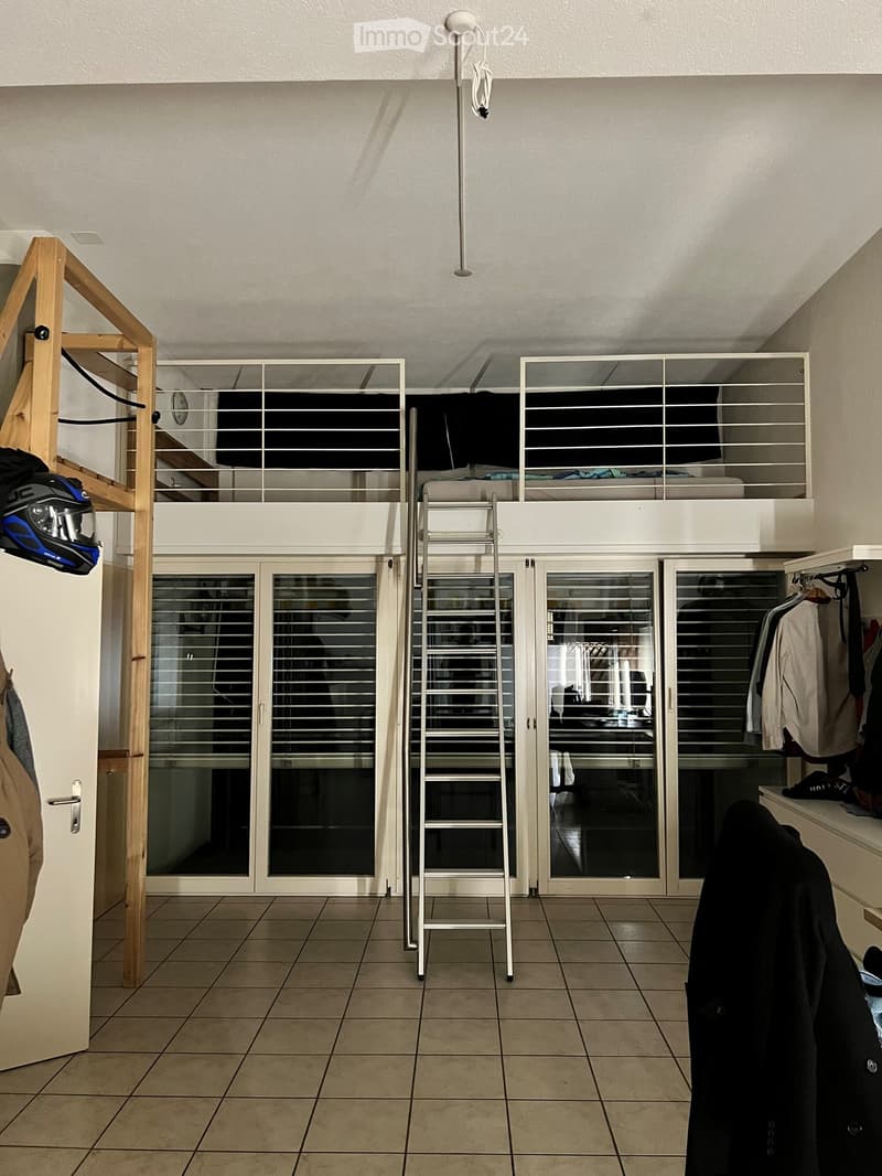 A multi-level room with a ladder leading to an upper loft area, tiled floor, and clothing hanging on a rack.