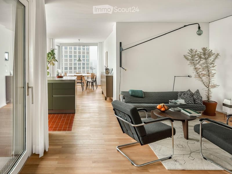 Modern living room with a grey sofa, coffee table, chairs, dining area, and large windows with a city view.