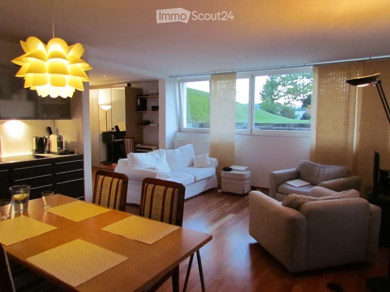dining table with chairs, 2 couches, white sofa with cushions, white ottoman, floor lamp, large windows, kitchen in background