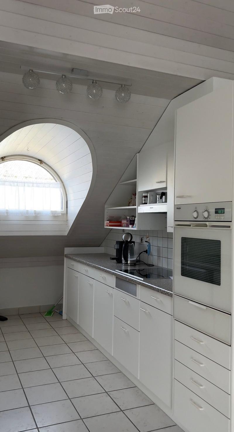 Modern kitchen with white cabinets, granite countertop, built-in oven, coffee maker, and shelves. Features a skylight window and pendant lights.