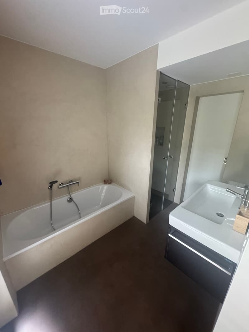 Modern bathroom with a bathtub, sink, and shower stall. Features a sleek design with a dark floor and light walls.
